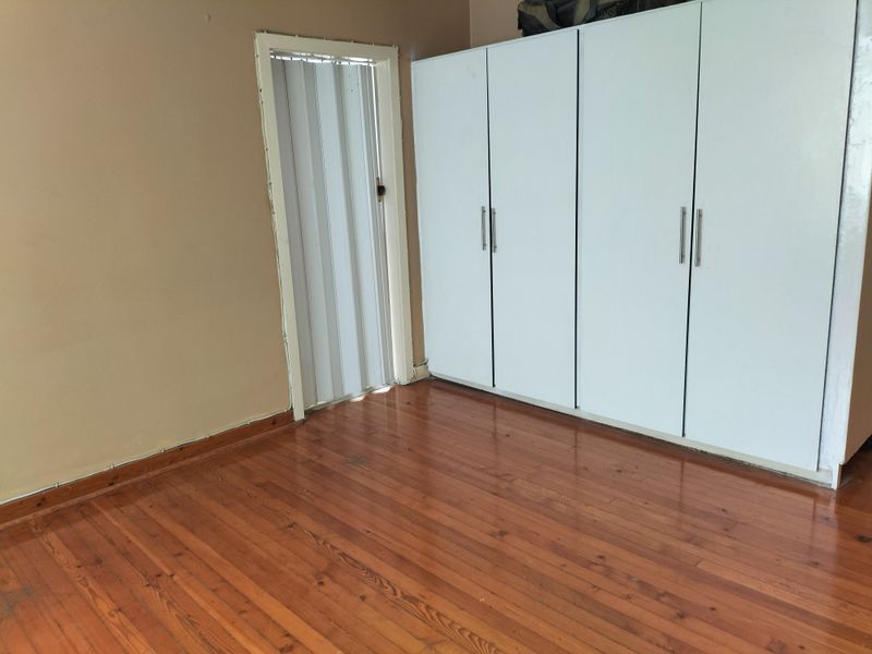 A bedroom featuring polished timber flooring, built-in white cupboards, and a folding door, presenting a clean, vacant space ready for personalization.