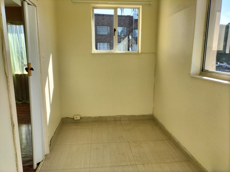 An empty bedroom featuring tiled flooring and aluminium window frames, offering a blank canvas for potential interior design updates.