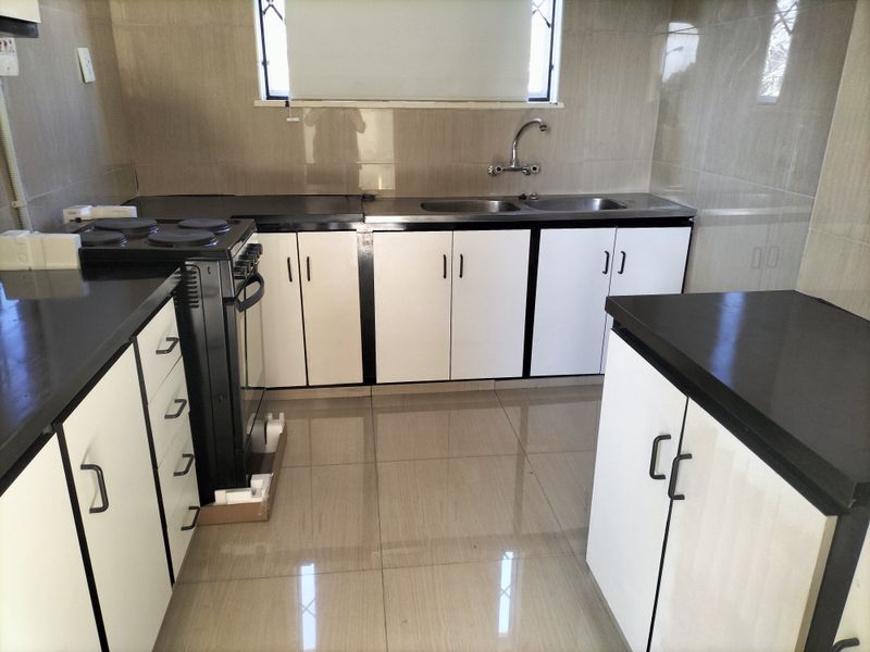 A functional kitchen featuring white cabinetry, dark countertops, a double sink, and tiled finishes throughout.