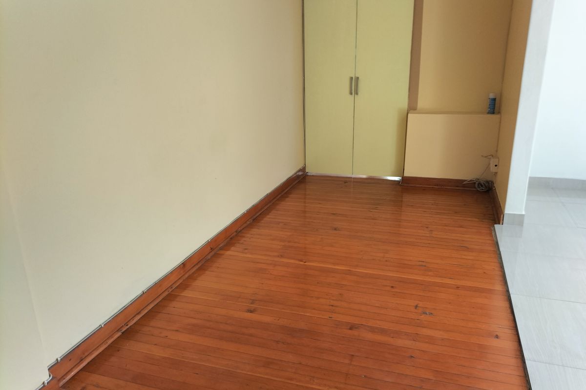 An empty bedroom featuring polished timber flooring and a built-in cupboard with light-colored doors.