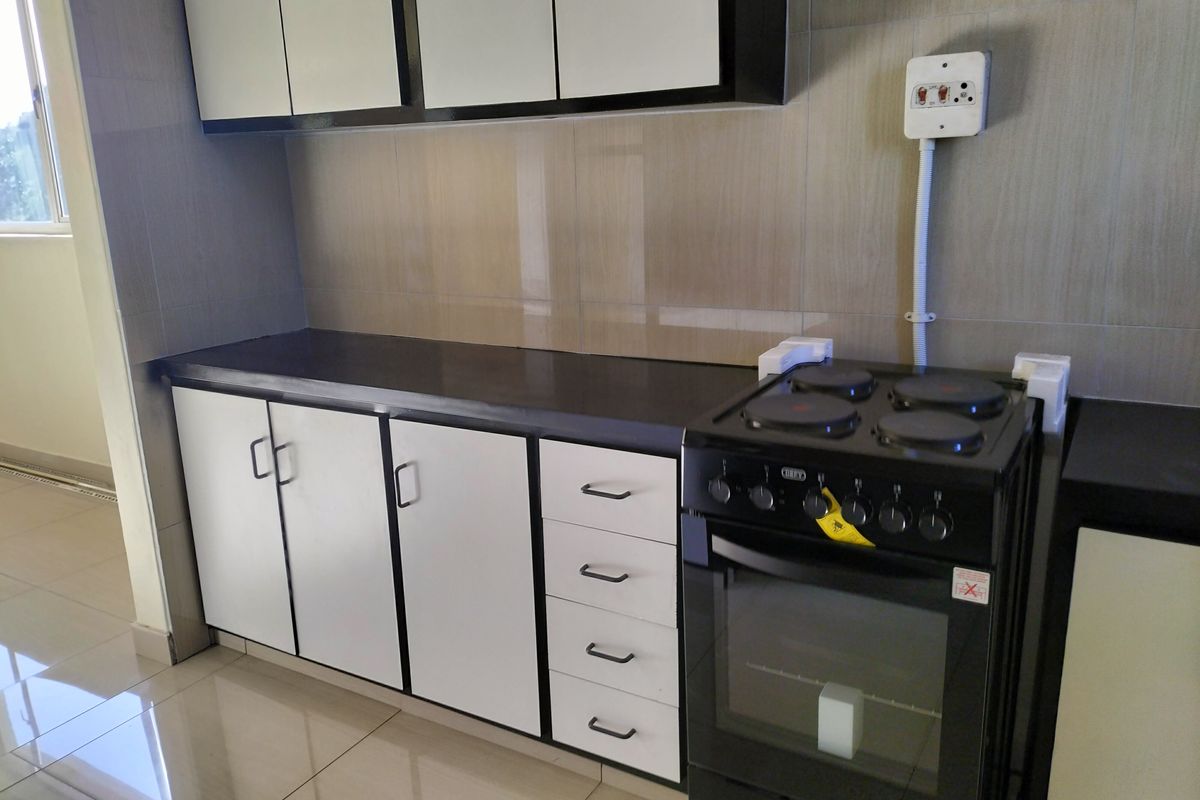 A clean, modern kitchen featuring white cabinetry, dark countertops, tiled backsplash, and a freestanding electric stove with exposed electrical wiring.