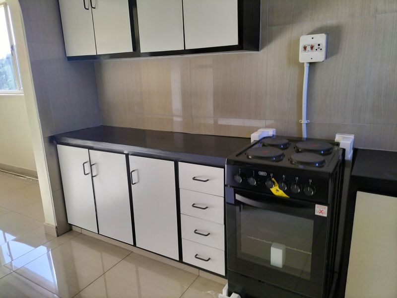 A clean, modern kitchen featuring white cabinetry, dark countertops, tiled backsplash, and a freestanding electric stove with exposed electrical wiring.