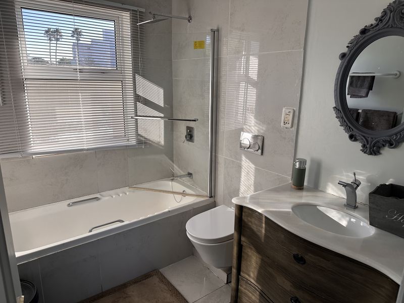 Modern bathroom featuring a built-in bathtub with a glass shower screen, wall-hung toilet, and a vanity cabinet with an integrated basin.