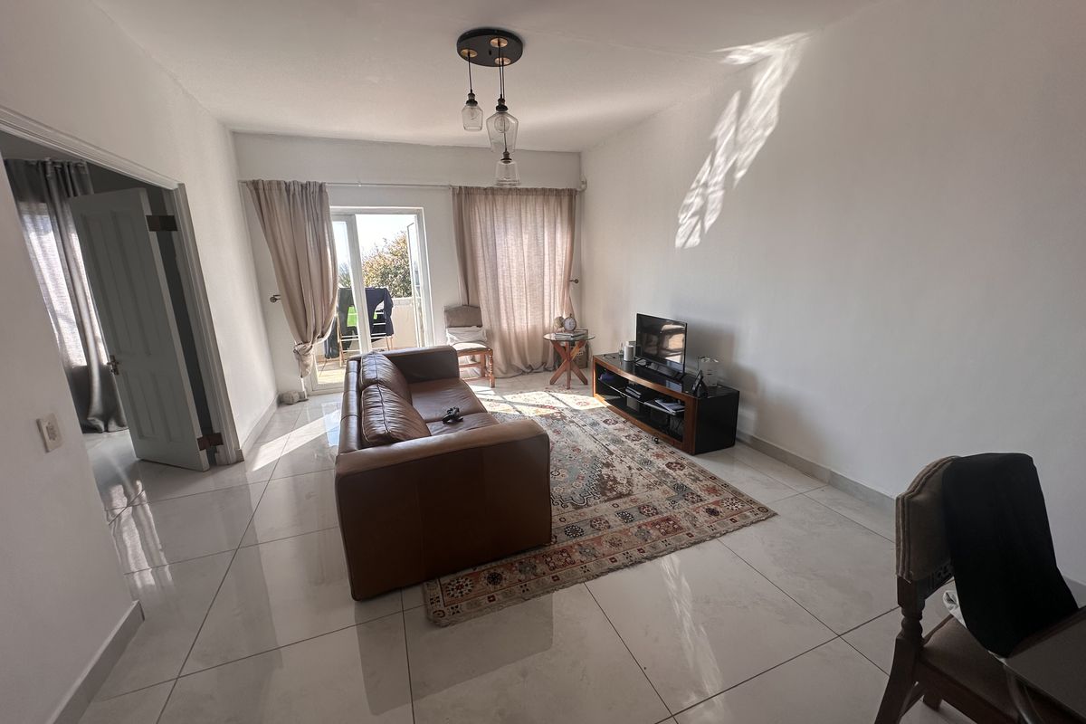 A bright living room featuring large format floor tiles, modern pendant lighting, and direct access to an outdoor balcony through a glass sliding door.