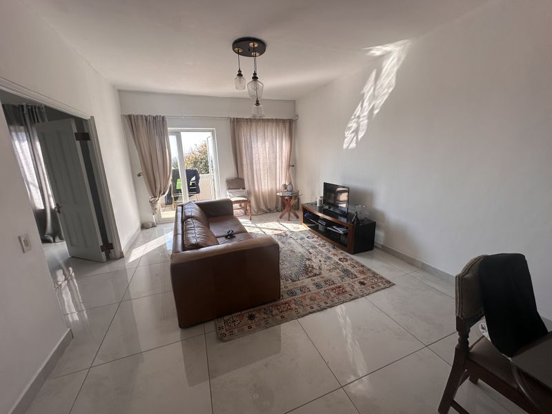 A bright living room featuring large format floor tiles, modern pendant lighting, and direct access to an outdoor balcony through a glass sliding door.