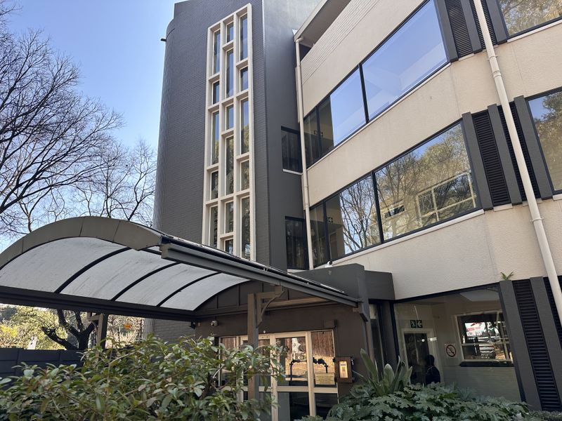 Modern apartment building entrance featuring a curved awning, large glass windows, and a distinctive vertical multi-pane window design.