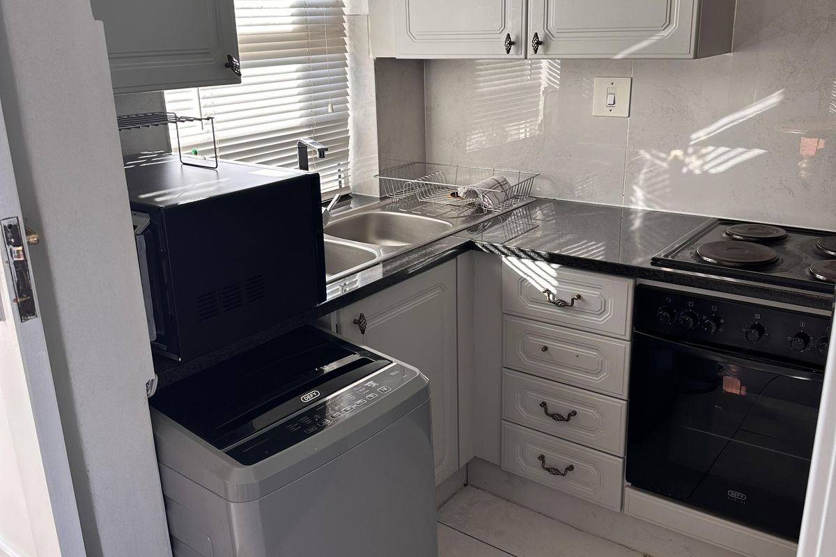 Compact kitchen featuring white cabinetry, granite countertops, built-in oven and hob, double basin sink, and tiled flooring.