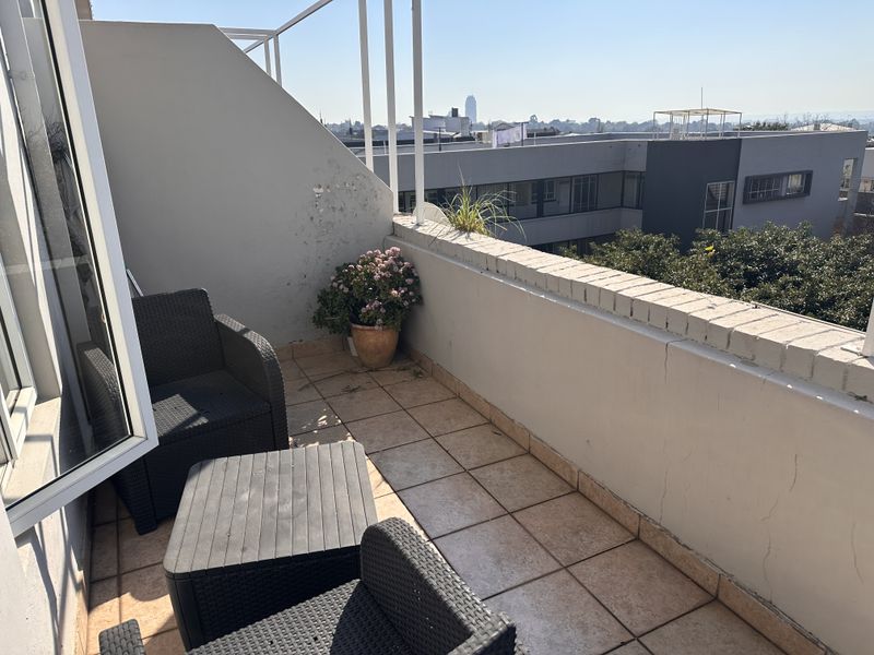 An outdoor balcony featuring tiled flooring and a brick parapet wall with views of the surrounding neighborhood.