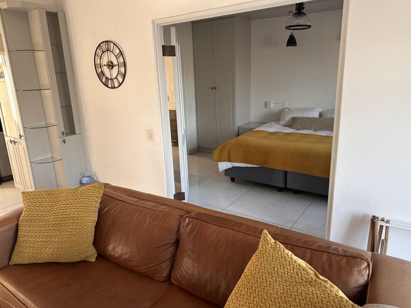 A bedroom featuring built-in cupboards, tiled flooring, and pendant lighting, accessible through a wide doorway from the adjacent living area.