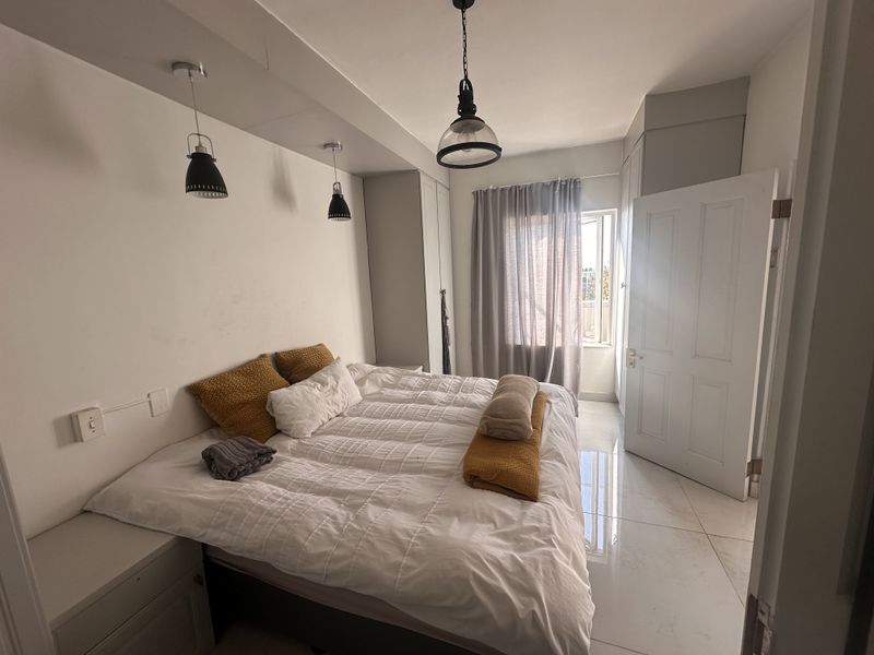 A well-lit bedroom featuring built-in cupboards, tiled flooring, and modern pendant lighting, offering a clean and functional living space.