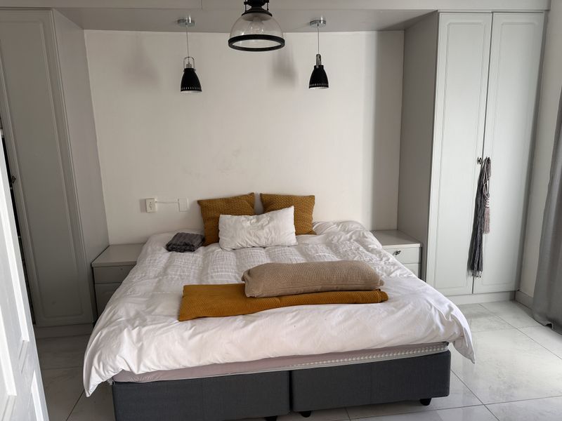 A well-lit bedroom featuring built-in cupboards, integrated bedside tables, and modern pendant lighting, finished with clean tiled flooring.
