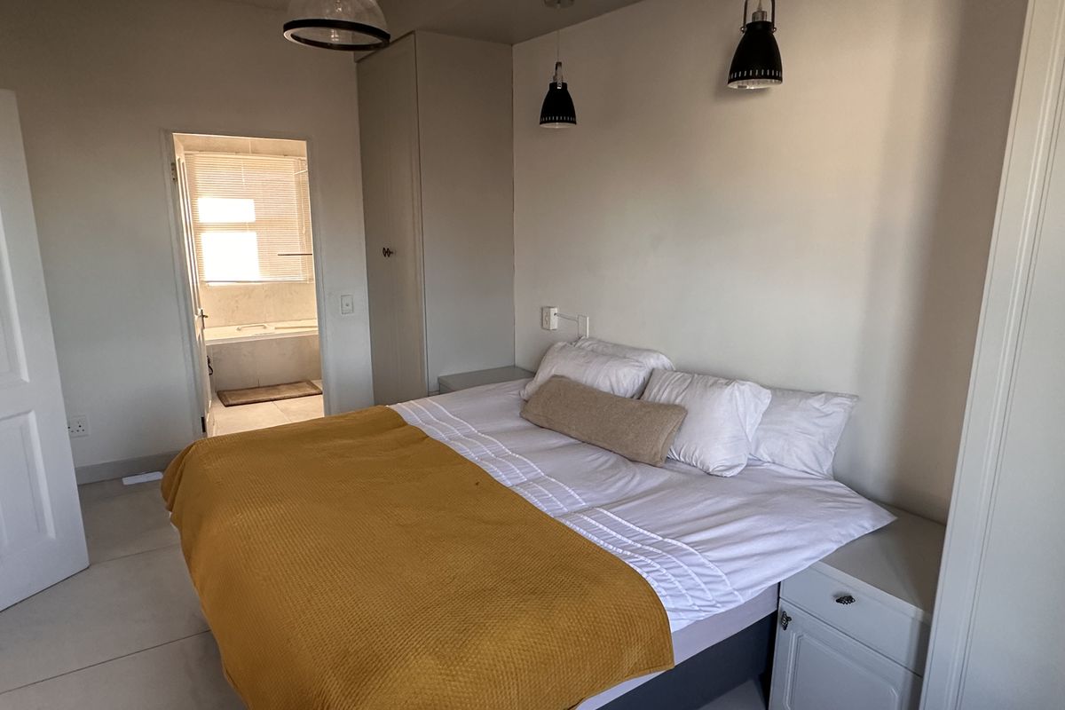 A well-lit bedroom featuring built-in wardrobes, modern pendant lighting, and tiled flooring, with direct access to an en-suite bathroom.