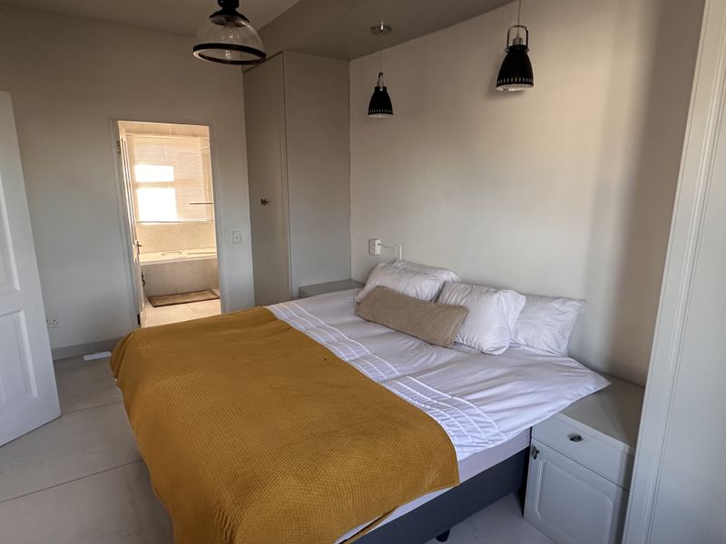 A well-lit bedroom featuring built-in wardrobes, modern pendant lighting, and tiled flooring, with direct access to an en-suite bathroom.