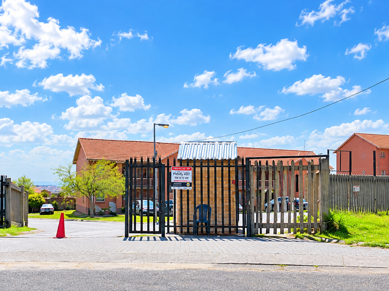 The entrance to the apartment complex features a secure gated access point with a guard house and perimeter fencing.