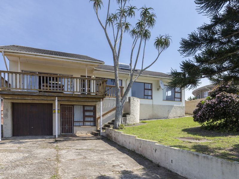 Front elevation of a two-story house featuring a wooden balcony, integrated garage, concrete driveway, and a landscaped garden area.