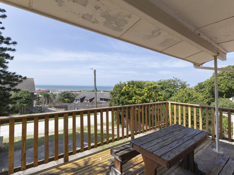 Covered outdoor balcony featuring wooden decking and balustrades, offering elevated views of the surrounding neighborhood and distant ocean.