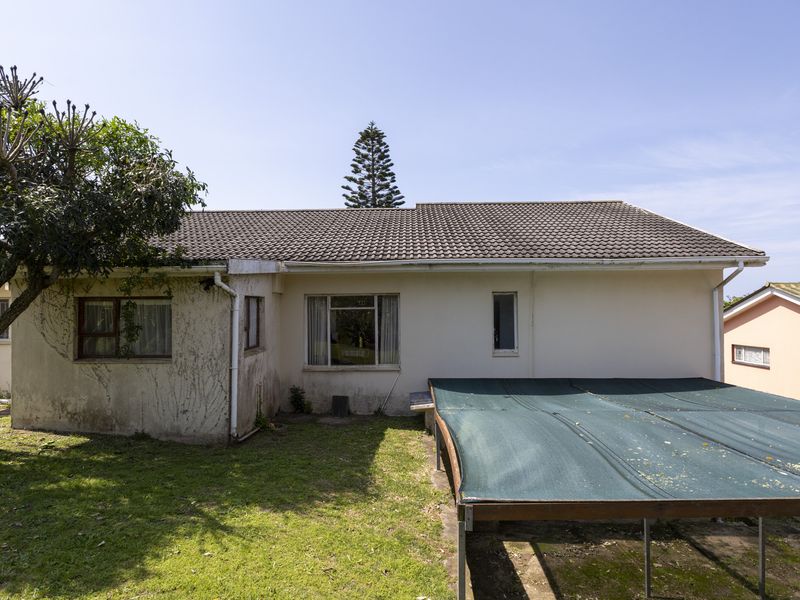 Rear view of the property featuring a tiled roof, aluminium window frames, and a basic shade cloth structure over a grassed backyard area.