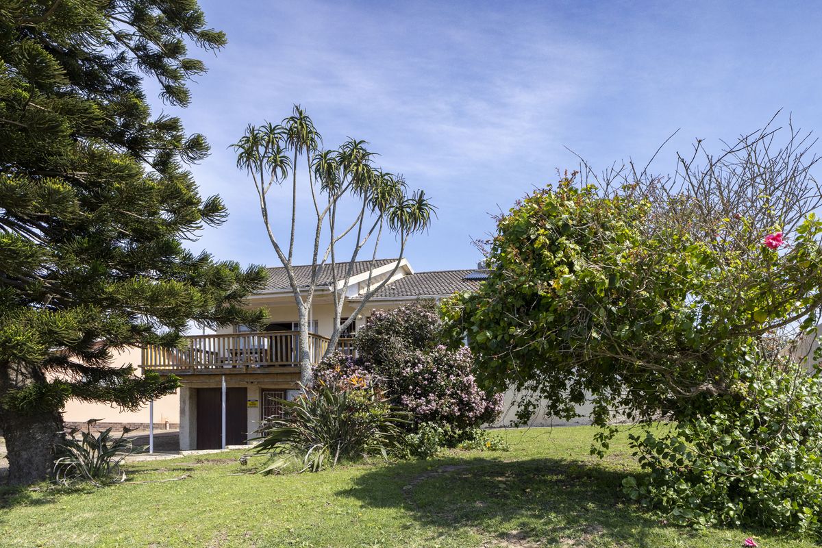 Rear view of the house featuring a wooden balcony, tiled roof, and established garden area.