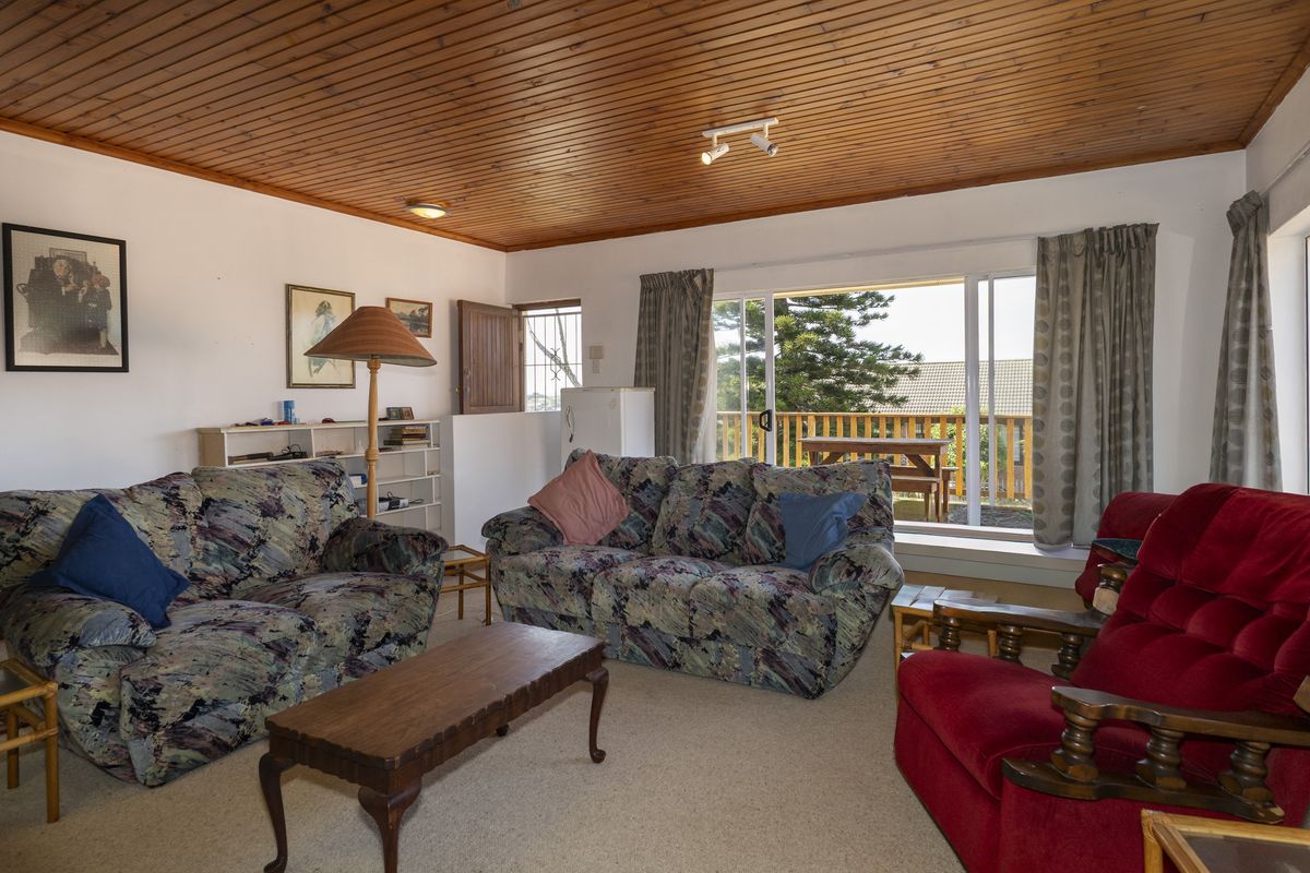 A living room featuring a timber tongue and groove ceiling, carpet flooring, and a sliding glass door providing access to an outdoor patio area.