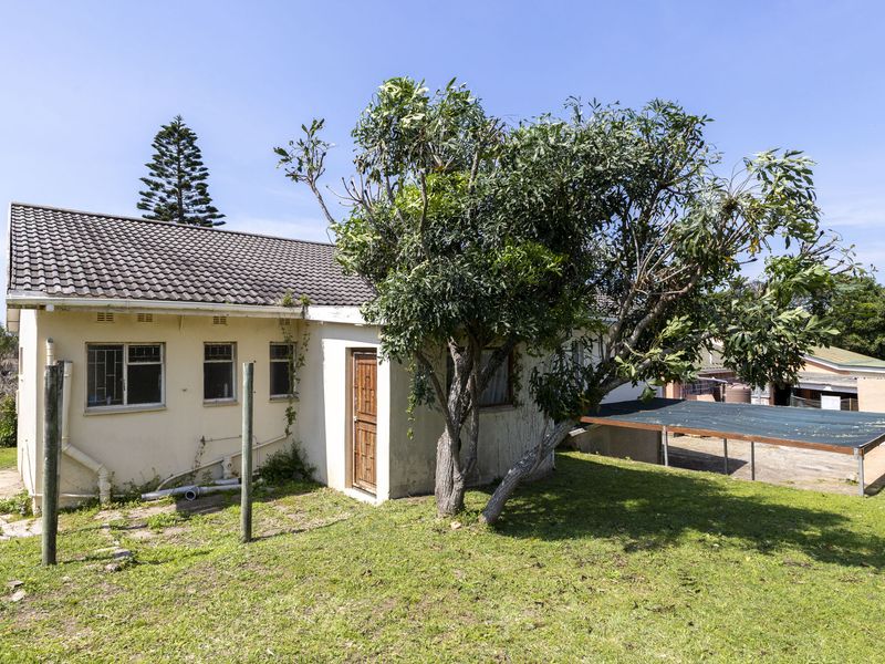 Rear view of the property featuring a tiled roof, plastered exterior walls, and a small shade cloth structure set within a garden area.