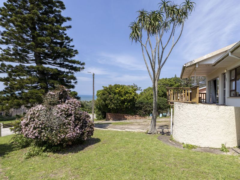 A rear view of the property featuring a wooden deck, landscaped garden, and exterior wall finishes with a view of the surrounding area.