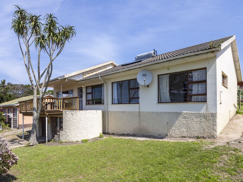 Rear view of the property featuring a raised timber deck, tiled roof, solar water heating system, and established garden area.
