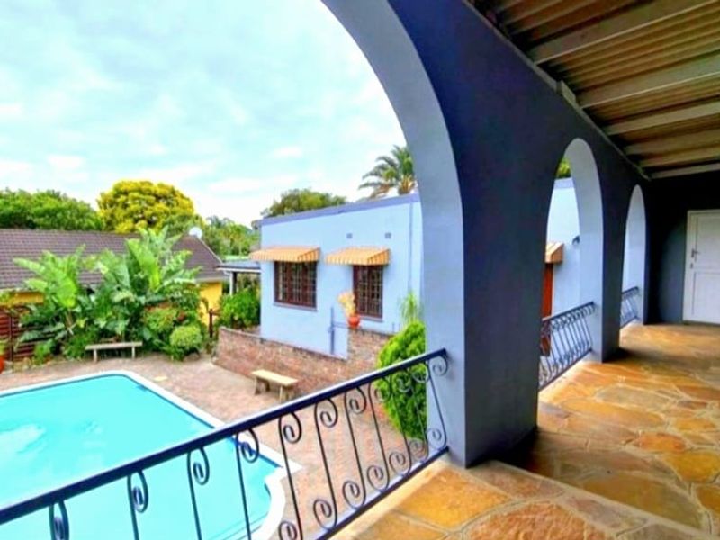 A covered patio featuring arched architectural details and stone flooring, overlooking a private swimming pool and garden area.
