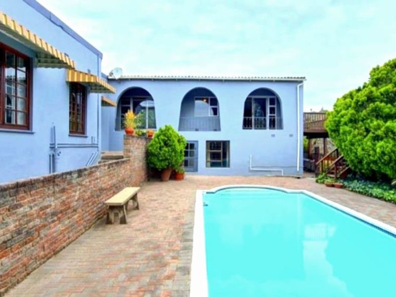 Rear exterior view featuring a swimming pool, brick paved patio area, and a blue-painted building facade with arched window detailing.