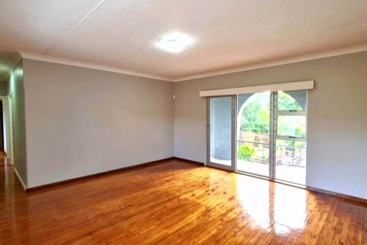 Spacious living area featuring polished hardwood flooring, neutral walls, and a large sliding glass door providing access to the exterior.