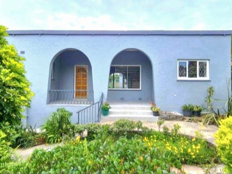 Front elevation of a single-story house featuring an arched porch, metal security gate, and established garden landscaping.