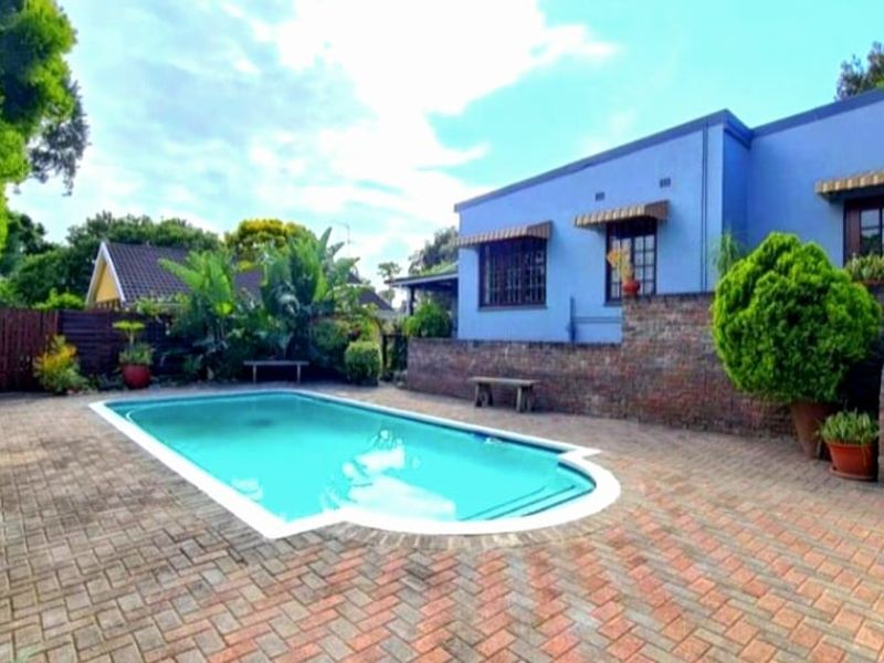 A well-maintained outdoor pool area featuring brick paving, a retaining wall, and a staircase leading to the rear of the house.