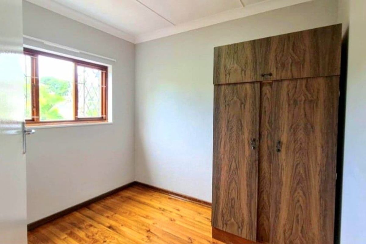 A clean, empty bedroom featuring polished timber flooring, neutral wall finishes, and a built-in wooden wardrobe.
