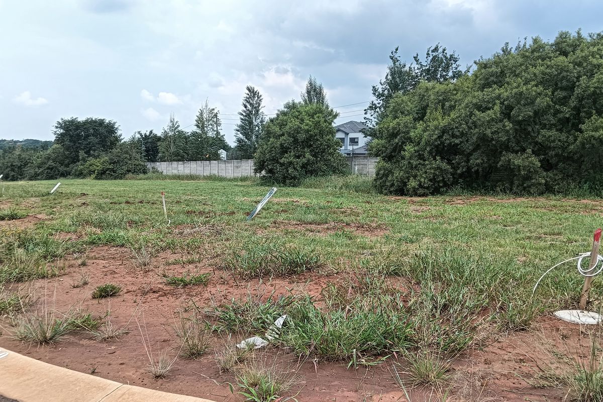 A vacant residential plot featuring natural grass cover, boundary markers, and a concrete curb, ready for development.