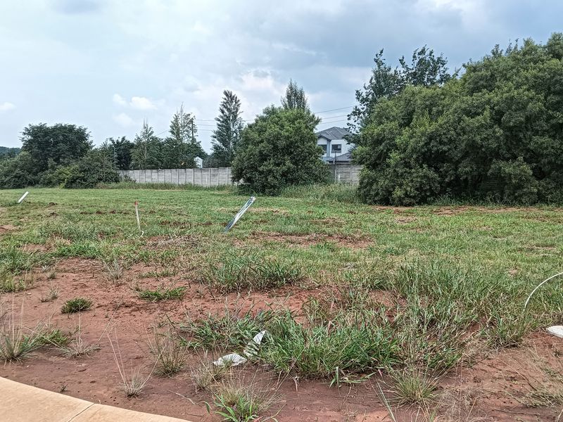 A vacant residential plot featuring natural grass cover, boundary markers, and a concrete curb, ready for development.