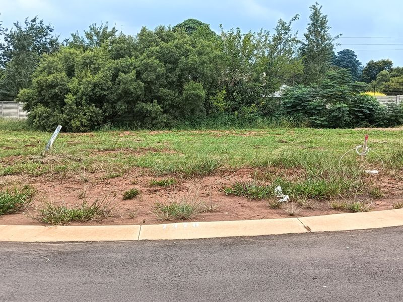 A vacant residential plot featuring a level grass surface, concrete curb, and established boundary wall, ready for development.