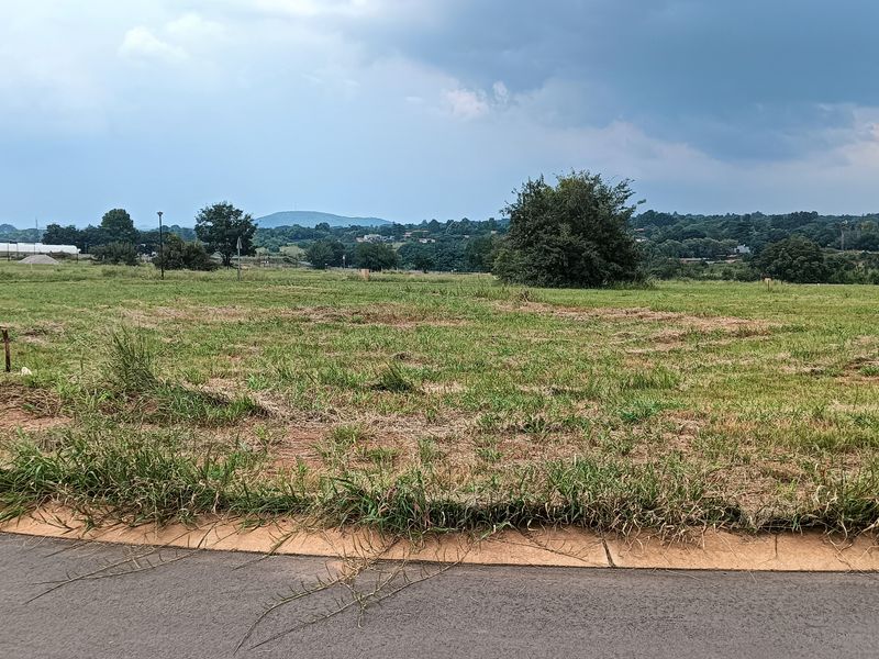 A vacant residential plot of land featuring open grassland with a paved road frontage and scenic landscape views.
