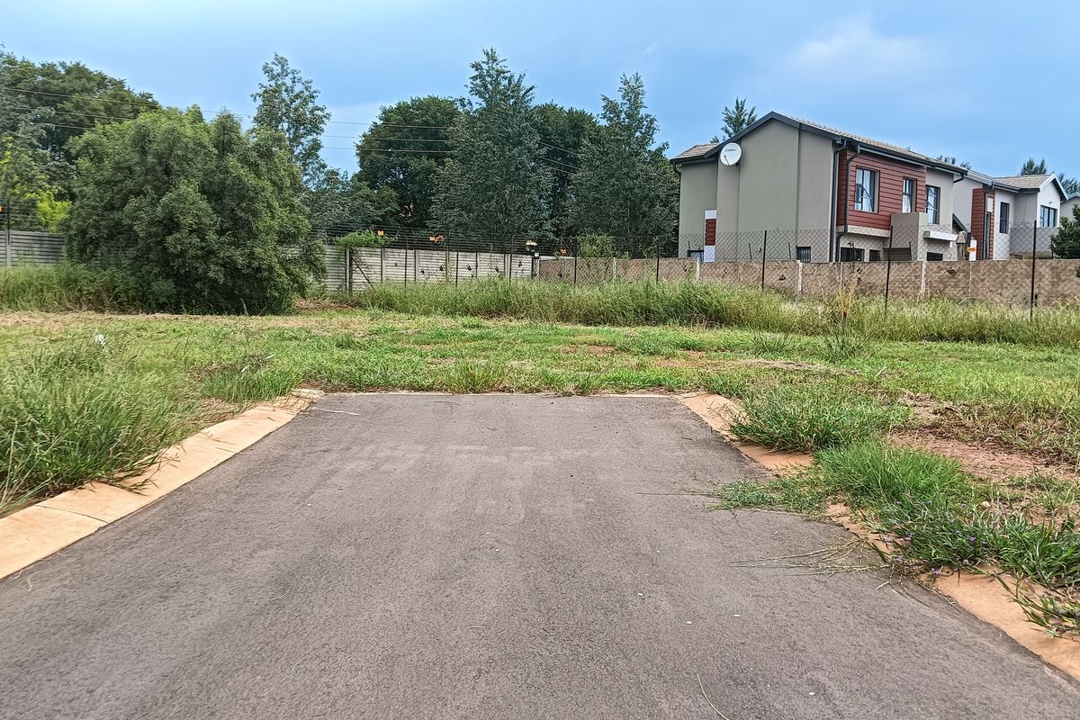 A vacant residential plot featuring a paved driveway entrance and perimeter fencing, situated in a developed neighborhood setting.