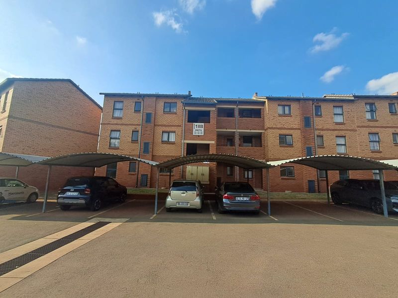 Front elevation of a multi-story brick apartment complex featuring covered parking bays and a paved driveway area.