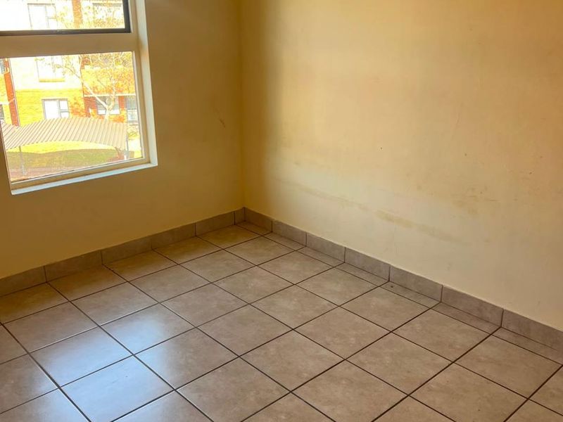 An empty bedroom featuring tiled flooring and a window with natural light, requiring minor cosmetic updates to the wall finishes.
