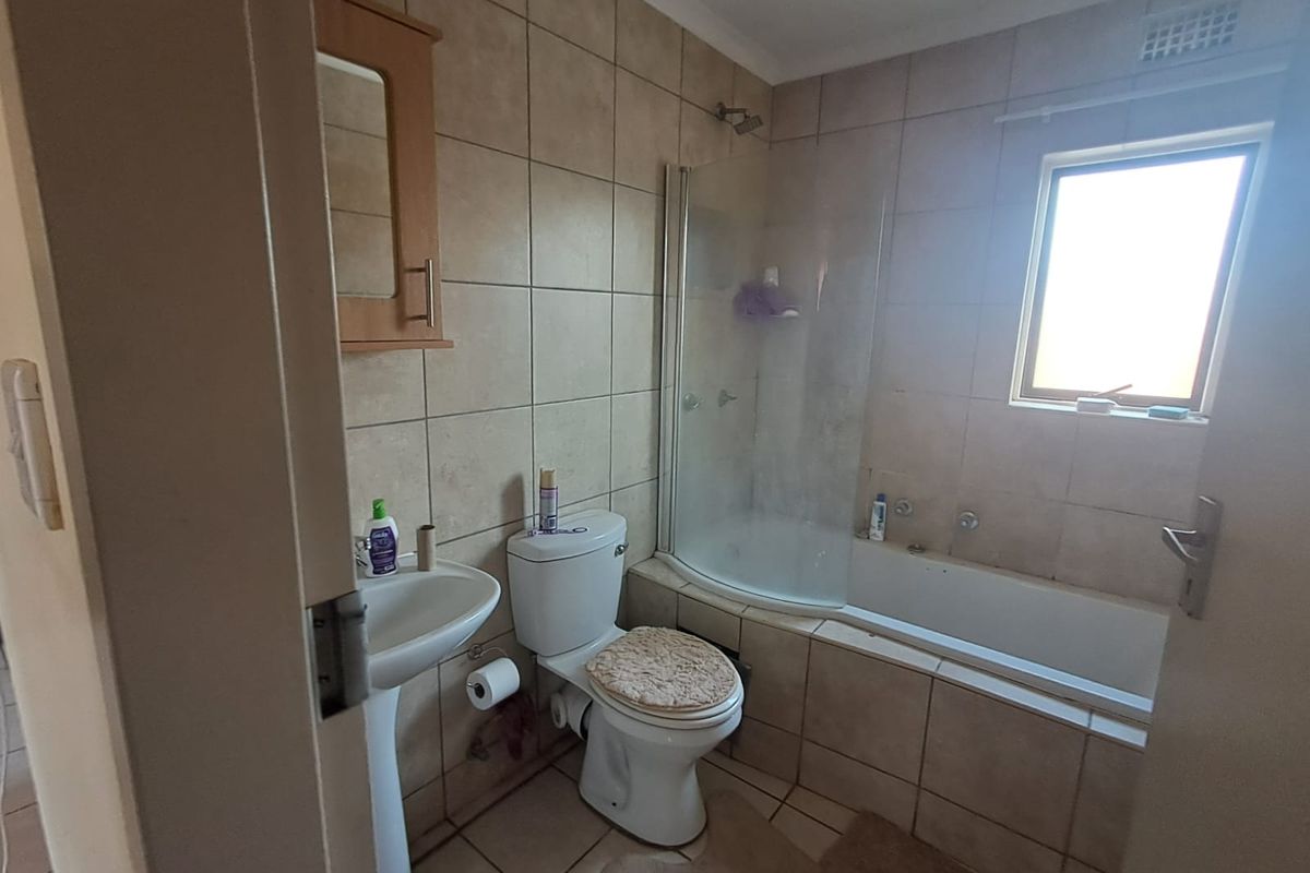 A functional bathroom featuring a pedestal basin, toilet, and a combined bathtub with a glass shower screen and wall-to-floor tiling.