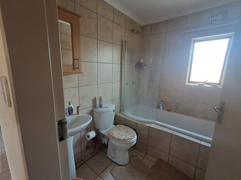 A functional bathroom featuring a pedestal basin, toilet, and a combined bathtub with a glass shower screen and wall-to-floor tiling.