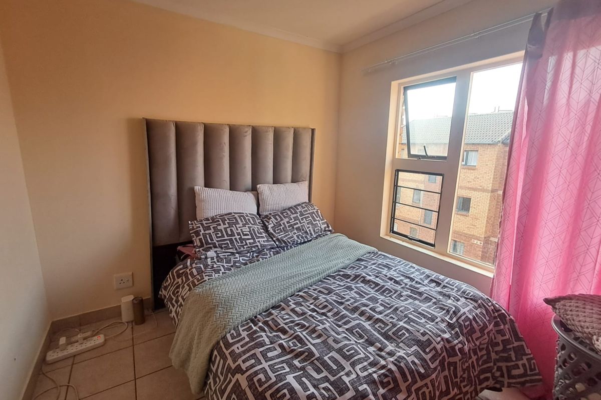 A functional bedroom featuring tiled flooring and a large window with security bars, providing natural light and views of the surrounding apartment complex.