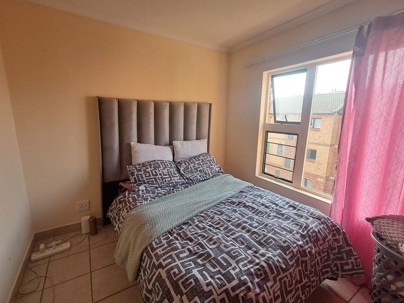 A functional bedroom featuring tiled flooring and a large window with security bars, providing natural light and views of the surrounding apartment complex.
