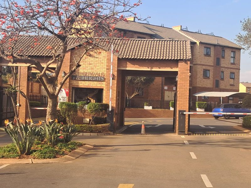 The main entrance to Boardwalk Heights apartment complex, featuring a brick security gatehouse, boom barriers, and paved driveway access.