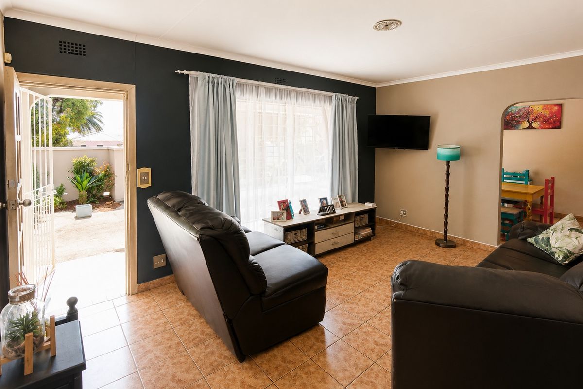 A living room featuring tiled flooring, a dark accent wall, and an archway leading to an adjacent space, with direct access to an outdoor area.