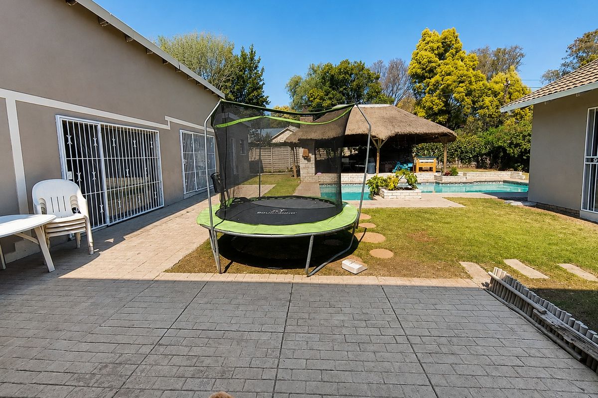 Rear garden area featuring a swimming pool, a thatched lapa entertainment space, and a paved patio area adjacent to the main house.