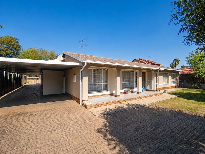 A single-story residential property featuring a paved driveway, attached carport, covered front patio, and a tiled roof.