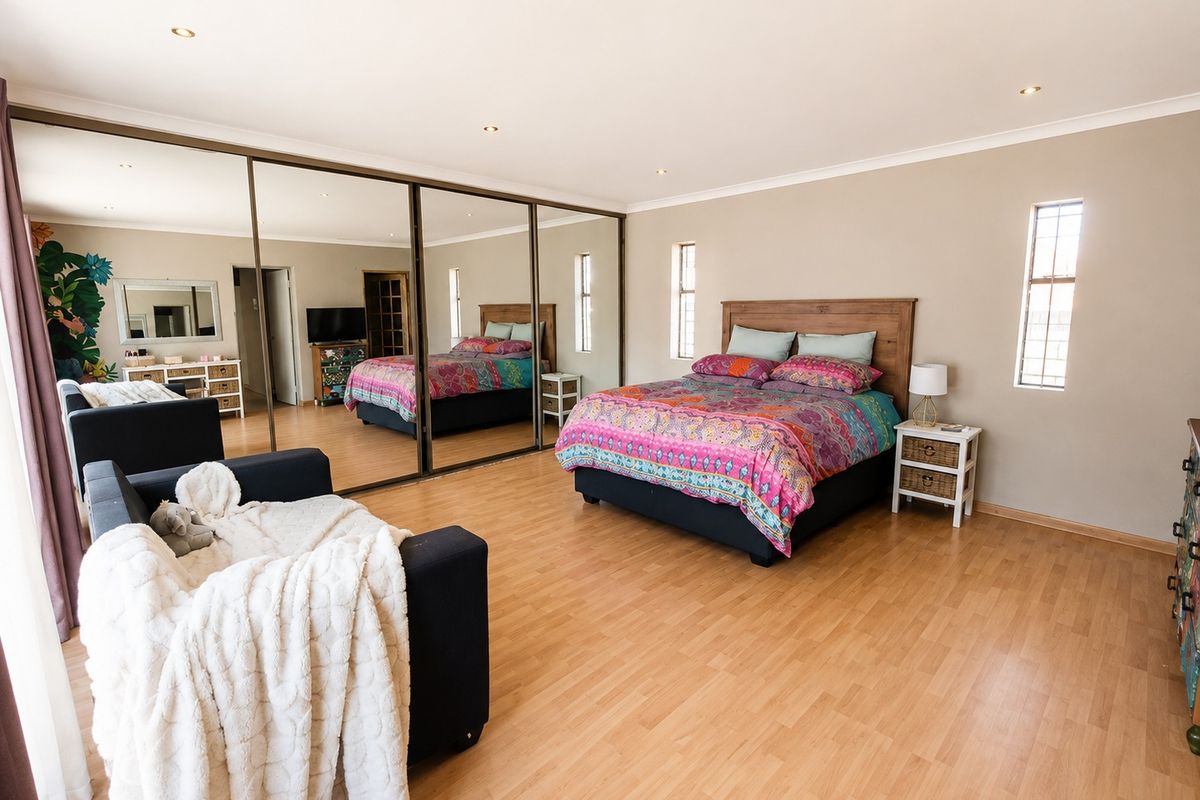 Spacious bedroom featuring laminate flooring, recessed downlighting, and extensive floor-to-ceiling mirrored built-in cupboards providing ample storage.