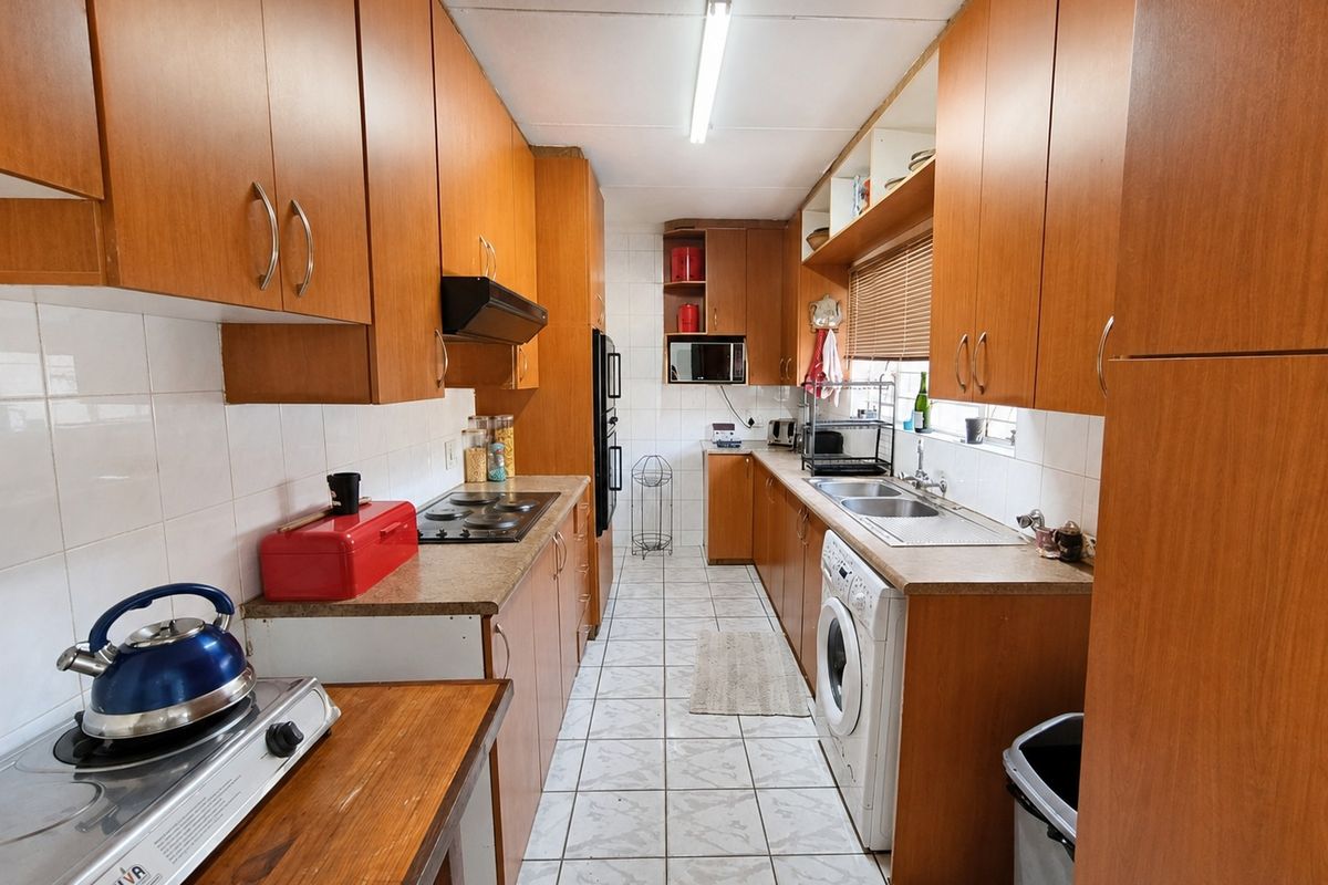 A functional galley-style kitchen featuring extensive wood-look cabinetry, built-in oven, electric hob, and tiled flooring with integrated laundry plumbing.