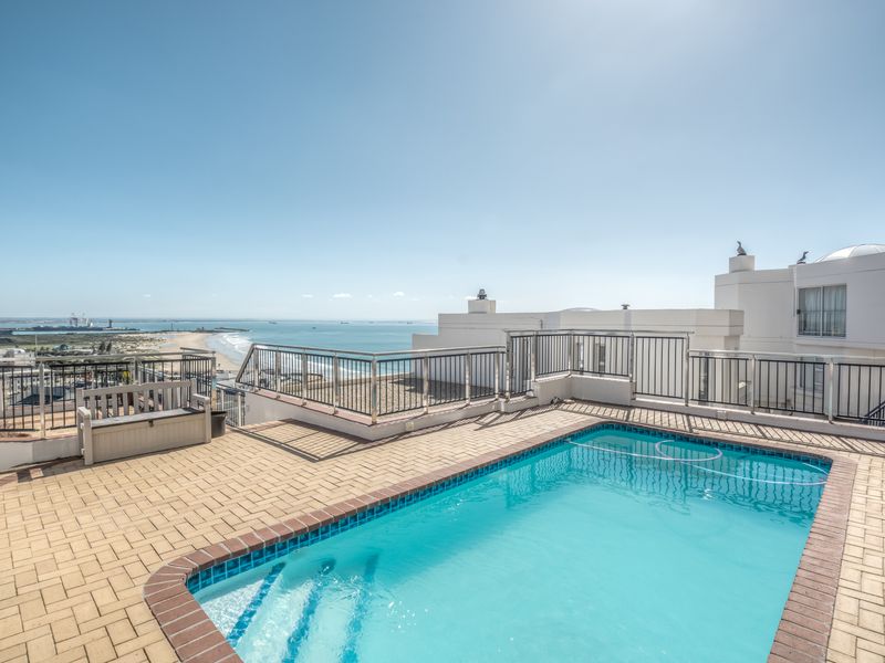 A rooftop swimming pool area featuring paved decking, metal safety balustrades, and expansive ocean views.